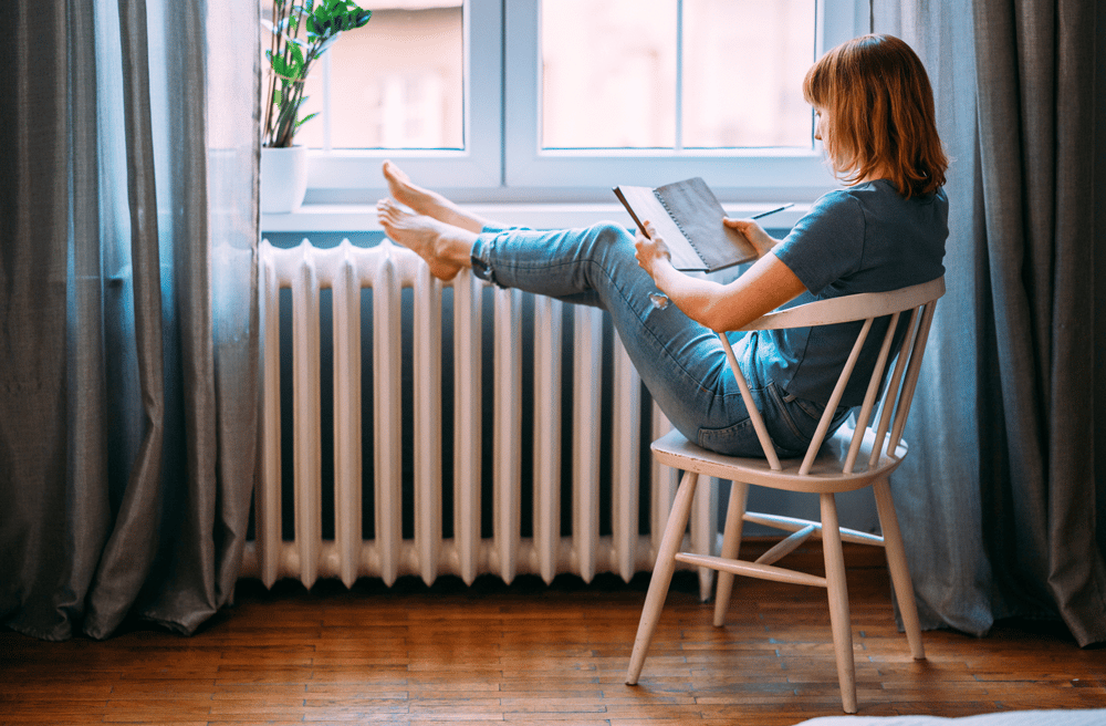 Femme en train de lire au chaud les pieds sur un radiateur