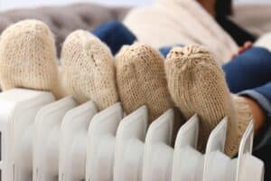 Personnes avec des chaussettes de laines épaisses se réchauffant les pieds sur un radiateur